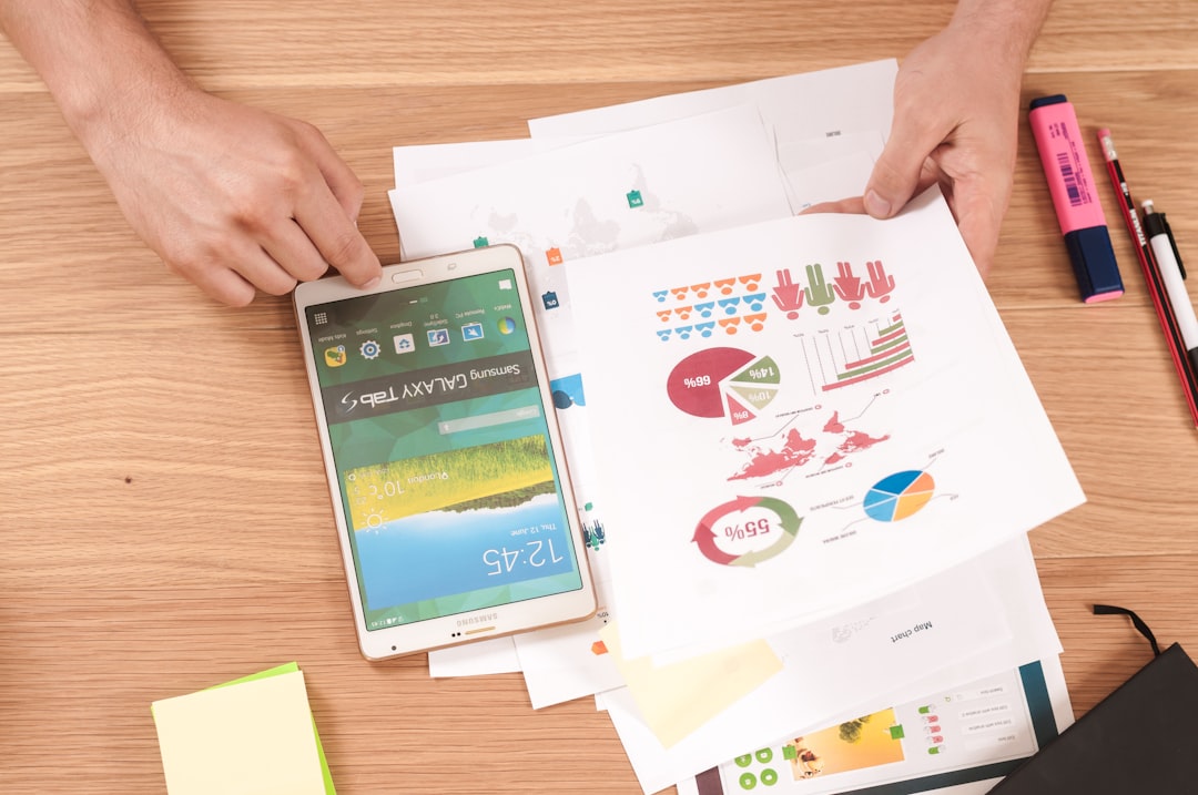 Hands holding a smartphone and reviewing printed charts and graphs, evaluating content ROI on a wooden table, with pens and sticky notes nearby.