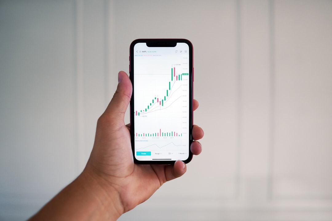 A hand holds a smartphone showcasing a financial chart with an upward-trending candlestick graph, illustrating the precision of AI decision-making, against a plain white background. AI Decision Making