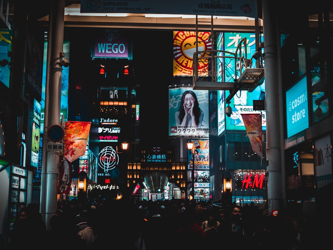 A busy city street at night with many people and brightly lit advertisements, billboards, and shop signs in Japanese showcases effective marketing strategies from brands like H&M and WEGO.