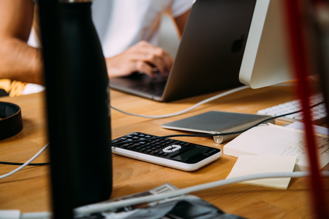 At a cluttered desk, a person types on a laptop, surrounded by papers, a calculator, and scattered stationery—an organized chaos that speaks volumes about their dedication to maintaining brand credibility.