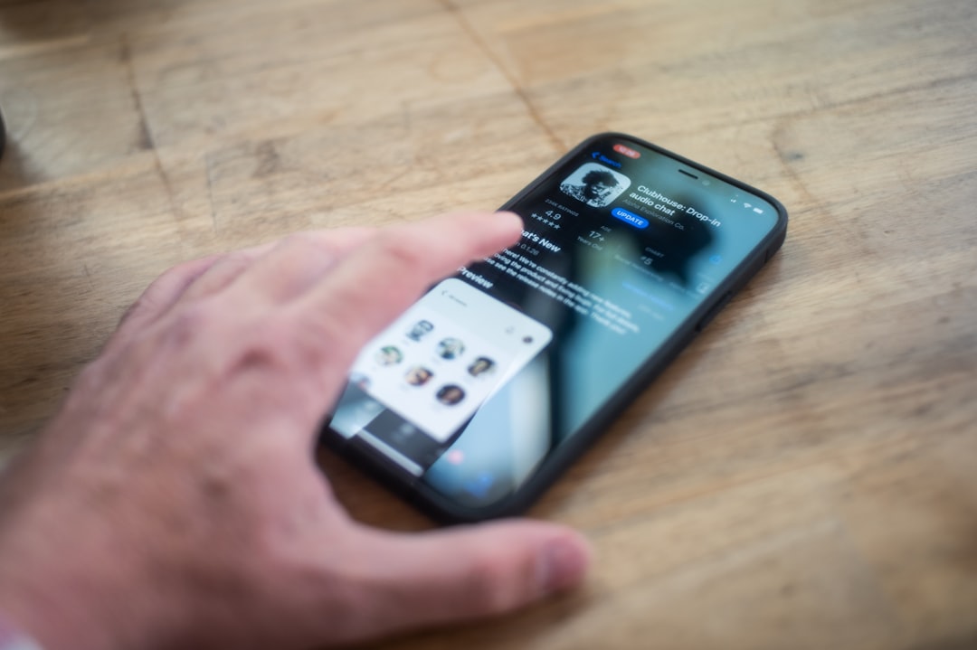 A person's hand interacts with an iPhone on a wooden table, displaying a social media app profile with small profile pictures visible below—an essential tool in modern crisis communications.