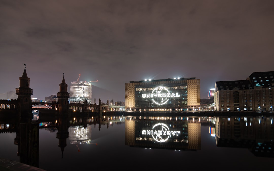 A night view of the city waterfront features the Universal logo projected on a building, crane, and bridge, symbolizing financial brand strength. The scene is beautifully reflected in the water, showcasing an ambience of prosperity and monetization.