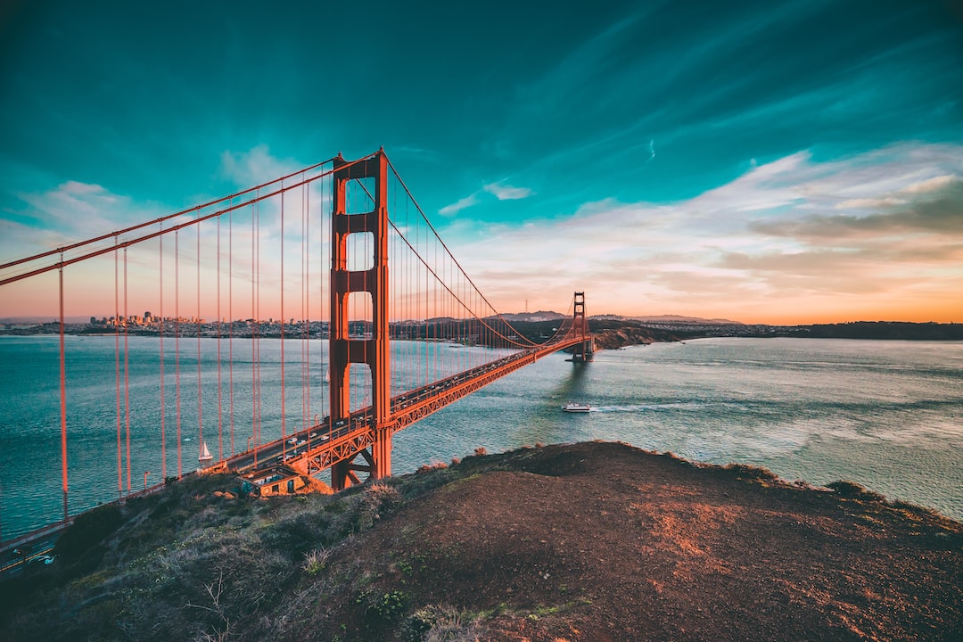 Golden Gate Bridge spans across the water at sunset, with a boat navigating regulatory challenges as it passes underneath and the city visible in the distance.