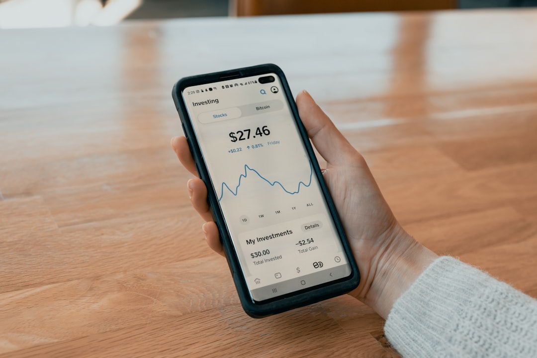 Person holding a smartphone displaying a stock market app interface, symbolizing fintech transformation and the shift toward mobile financial technology solutions. Digital Transformation in Fintech